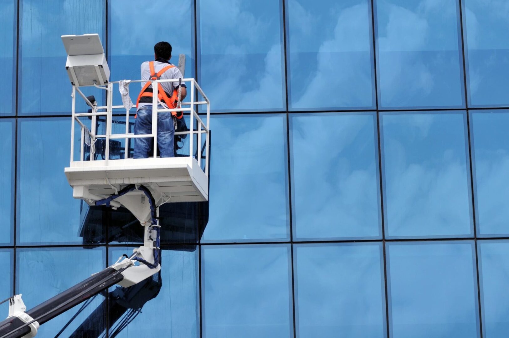 A man in a cherry-picker is cleaning the windows of a building.