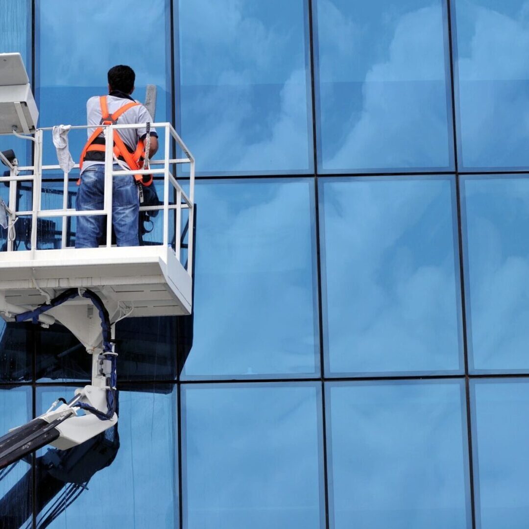 A man in a cherry-picker is cleaning the windows of a building.