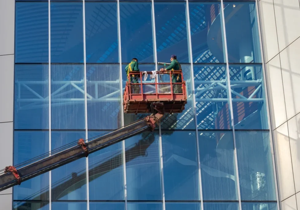Two men in a cherry-picker working on the side of a building.
